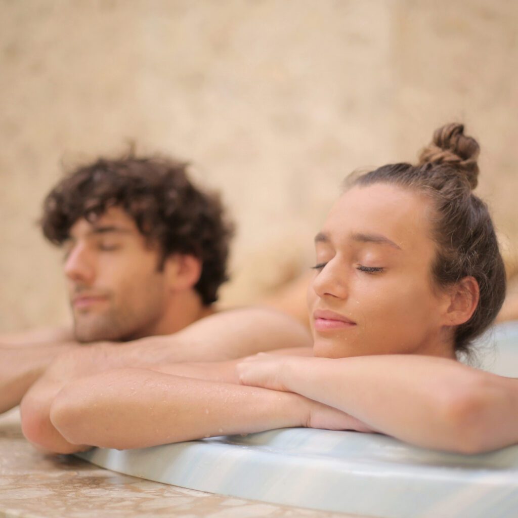 junger entspannter Mann und junge entspannte Frau mit geschlossenen Augen am relaxen im Wellnessbad.