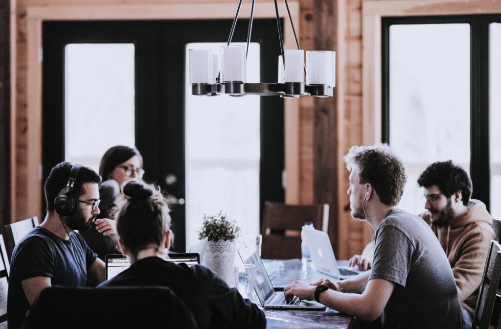 junge, moderne, konzentrierte Menschen sitzen an einem großen Arbeitstsich mit Laptops im Co-working Bereich.