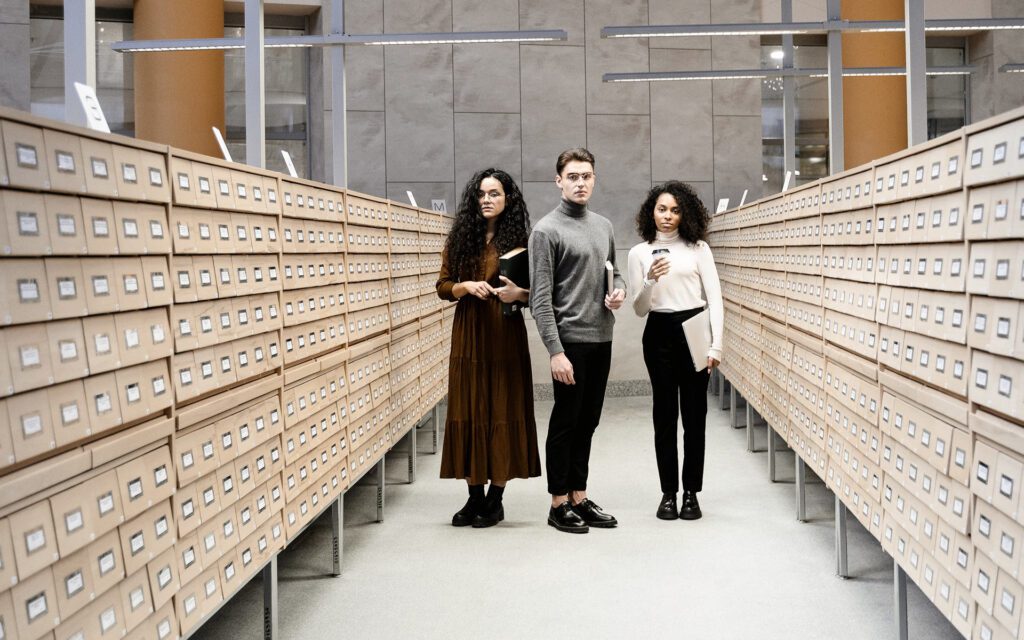 Drei junge moderne Menschen stehen in großem Archiv Raum